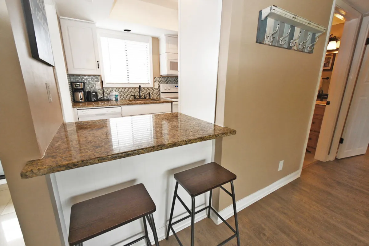 A welcoming kitchen scene with granite countertops, bar stools, and ample cabinetry. The warm lighting and inviting setup encourage casual dining and socializing.
