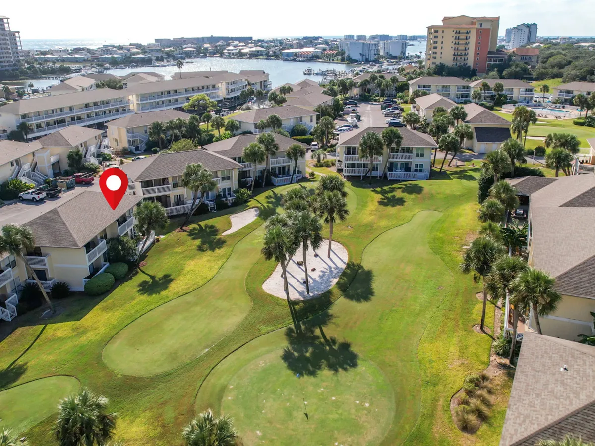 This image captures a sweeping view of Sandpiper Cove’s par-3 golf course, lined with palm trees and framed by a row of condominium buildings with private balconies. The distant view shows the marina and hints at water access, while the golf course itself demonstrates leisurely vacation activities and the proximity of the buildings to outdoor amenities.