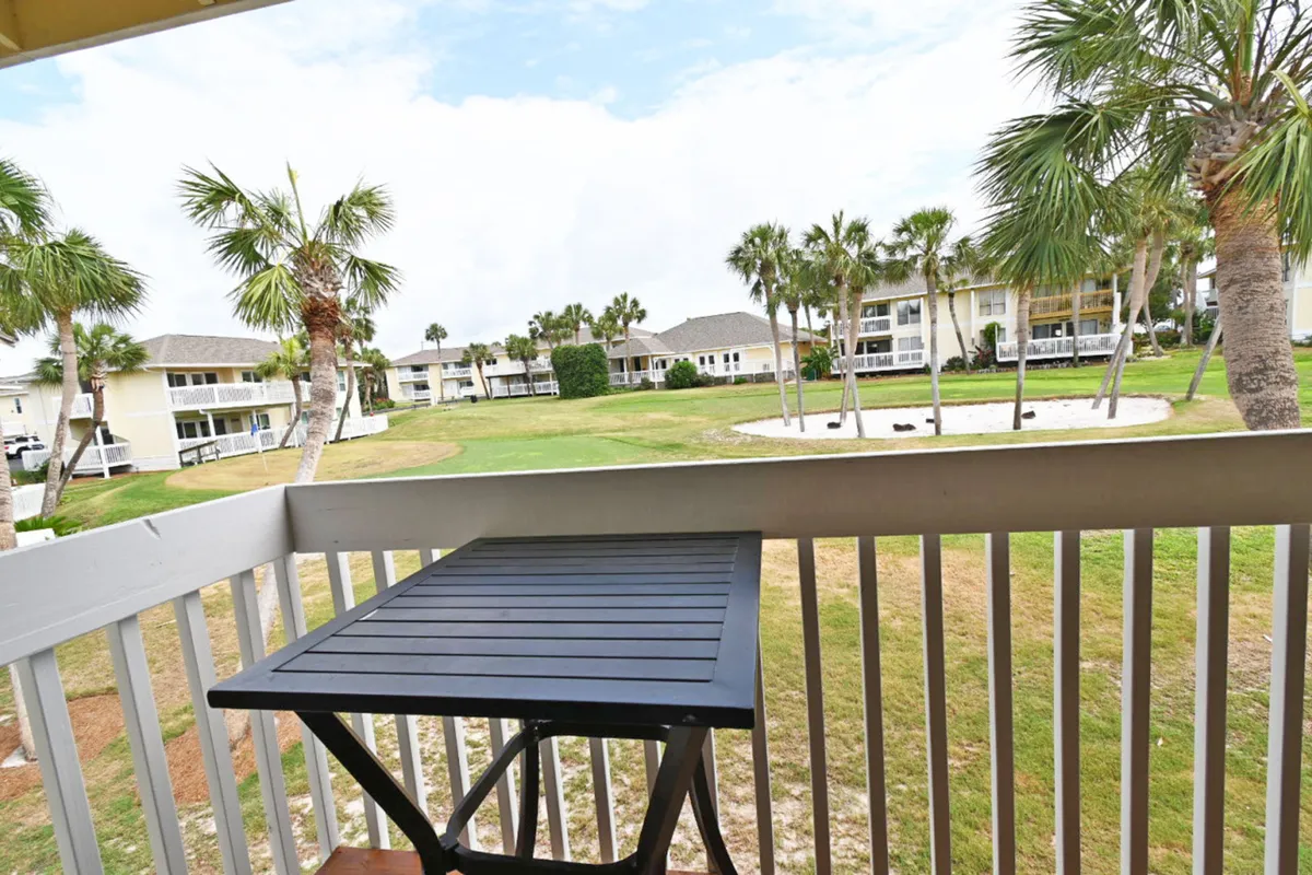 This exterior view highlights a private balcony with a table set for two, overlooking lush golf course greens and swaying palm trees, surrounded by neighboring condo buildings. The atmosphere is peaceful and inviting, ideal for leisurely moments outdoors.