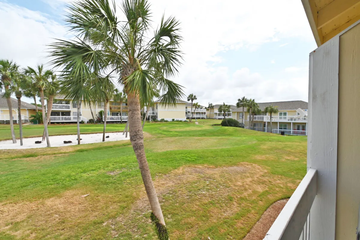 This exterior image shows a well-maintained par-3 golf course green with a sand bunker, flanked by palm trees and bordered by the balcony railing of a nearby condo. The scene is tranquil, with open, inviting green spaces perfect for golf and outdoor enjoyment.